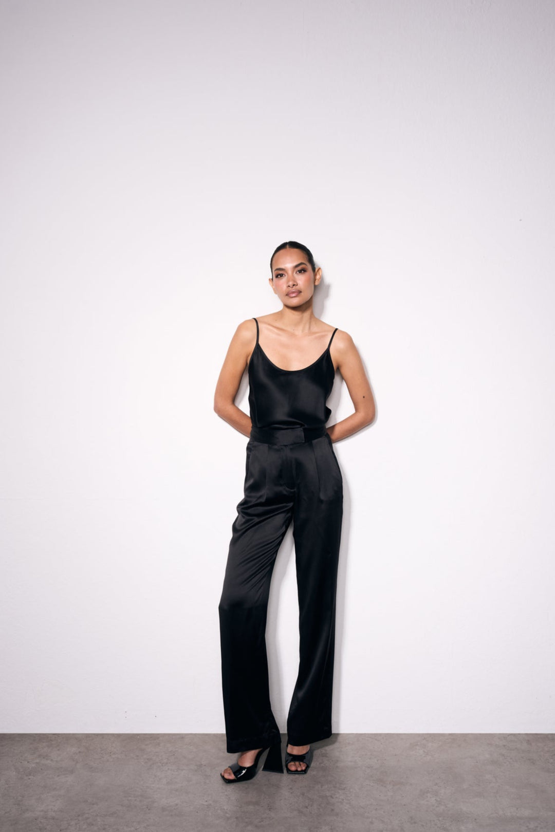 Model wearing black high-waisted silk trousers styled with coordinating silk top – ideal for monochrome outfits or occasionwear.